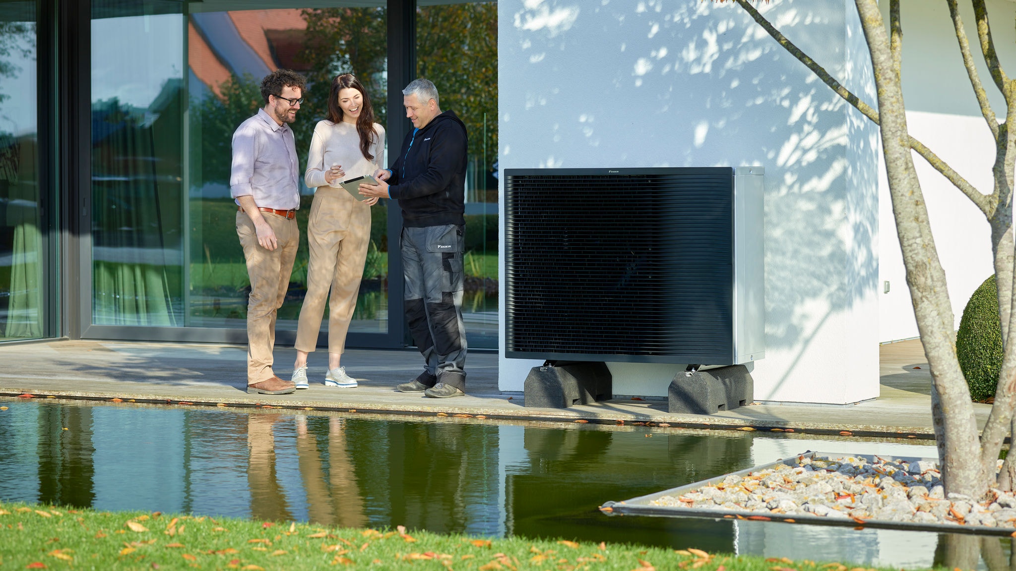 Ein Paar im Garten im Gespräch mit einem Installateur, neben dem Außengerät einer Daikin Altherma